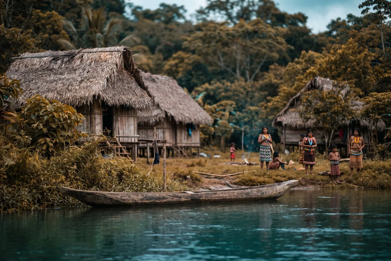 An indigenous village of thatched stilt huts with a dugout canoe along the riverbank